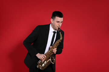 Naklejka premium Young man in elegant suit playing saxophone on red background