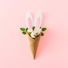 Creative layout made of bunny rabbit ears with flowers and ice cream cone on pastel pink background. Creative Easter holiday concept. Minimal style.