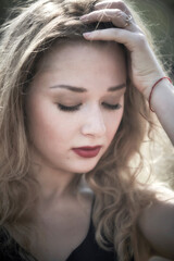 Portrait of a beautiful, healthy and attractive young woman with long blond hair and beautiful face with outdoor background. Female with red lips. Looking down