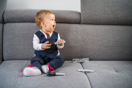 Cute little baby boy playing with toys while sitting on sofa.