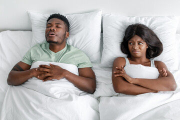Displeased unhappy millennial african american woman suffers from noise and snoring of sleeping...