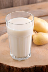 Vegan potato milk in a glass and potato tubers on brown wooden background. Close up. Plant based alternative milk replacer and lactose free, Trendy healthy vegetarian and vegan drink concept