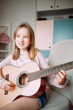 a cute little girl in a pink sweater is playing a baby guitar in her room. music training