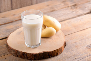 Vegan potato milk and potato on brown wooden background close up. Plant based alternative milk replacer and lactose free