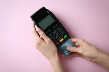Woman with credit card using modern payment terminal on pink background, top view