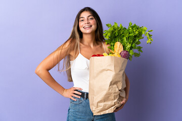 Young woman holding a grocery shopping bag posing with arms at hip and smiling