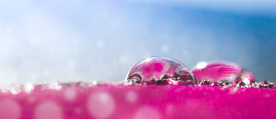 Drops of water on a pink surface against a blue background in the sun's rays.