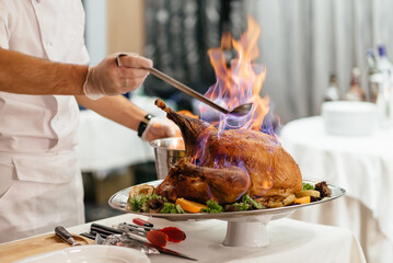 Turkey meat on fire on a platter with vegetables in a restaurant. The chef puts on a show for guests with burning meat. A restaurant dish with a beautiful presentation. Delicious meat dish for guests
