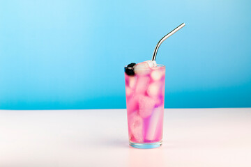 Summer refreshing pink cocktail with ice cube, metal straw and blackberry on blue background.