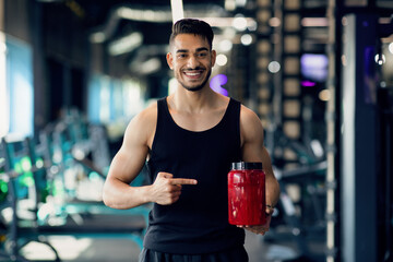 Bodybuilding Nutrition. Happy Arab Sportsman Pointing At Red Contrainer With Whey Powder