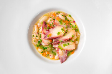 Overhead shot of a still life of octopus with white beans and vegetables on a white plate. Concept of traditional Spanish gastronomy.