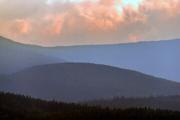 Zachmurzone, wieczorne niebo, zabarwione światłem zachodzącego słońca na czerwono nad szczytami odległych wzgórz.