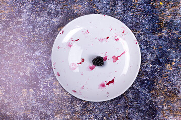 One blackberry on dirty plate with remnants of berries on dark background.