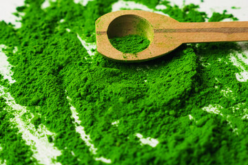 Close up of green powder and wooden spoon on white background.