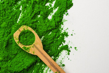 Close up of green powder and wooden spoon on white background.