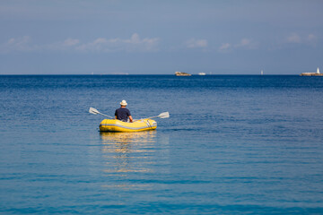 Mann von hinten mit Strohhut in gelbem Gummiboot am Meer unterwegs blickt zum Horizont