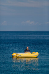 Digitaler Nomade sitzt in gelbem Gummiboot am Meer und arbeitet am Laptop, Hochformat