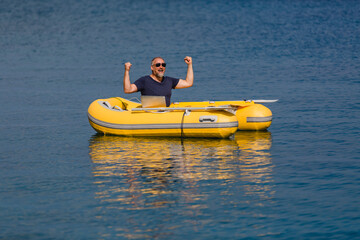 Digitaler Nomade mit Sonnenbrille und Laptop sitzt in gelbem Gummiboot am Meer, Emotionen Freude &...