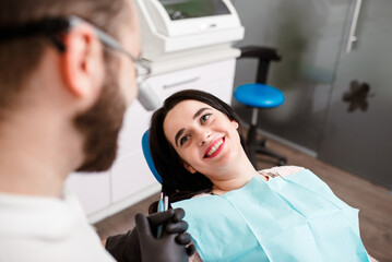 Fototapeta premium A young woman sitting in the dentist s chair frightened, she is holding the dentist s hand not allowing her to give her anesthesia.She gets terrified when she sees anesthesia coming out of the needle.