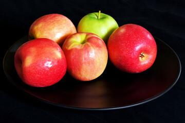 Fresh apples on a black porcelain plate on black background.