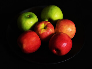Fresh apples on a black porcelain plate on black background.
