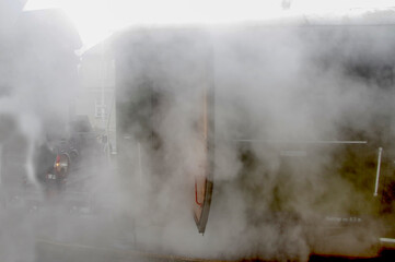 Obrazy na Plexi  Stary, zielony wagon kolejowy ciągnięty przez parowóz pozostawiający za sobą obłoki pary.