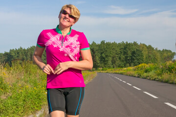Uśmiechnięta, atrakcyjna kobieta w ubraniu sportowym, stojąca na asfaltowej drodze.