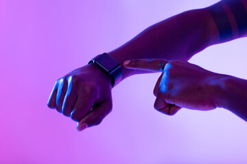 Cropped view of African American guy using smartwatch with blank screen in neon light, mockup