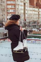 Young curly-haired woman in a beret with ice skates looks down at the ice rink