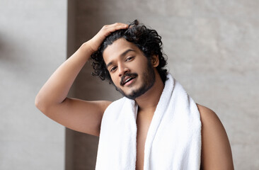 Male morning routine. Handsome indian man with towel on shoulder standing in bathroom, copy space