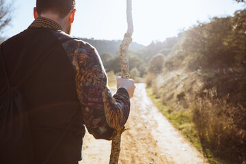 an with black sweatshirt and sleeves with flowers leaning on a wooden stick to be able to walk along a dirt road at sunset.