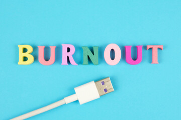 Word burnout from multi colored wooden letters and usb plug on blue background. Burnout metaphor....
