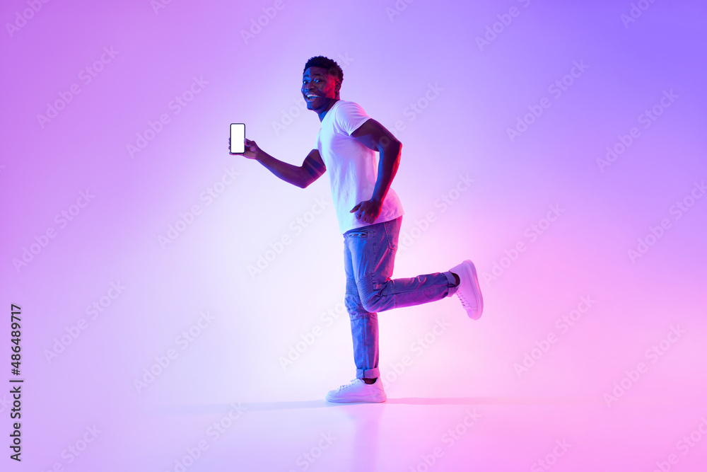 Poster excited young black guy with smartphone running in neon light, showing mockup for design on mobile d