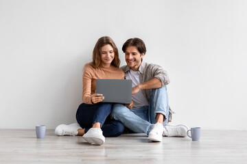 Smiling young european couple sitting on floor, resting from moving at house, searching idea for...