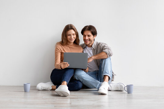 Smiling young european couple sitting on floor, resting from moving at house, searching idea for new interior