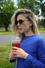 Blonde girl in sunglasses drinks an effervescent cocktail through a straw