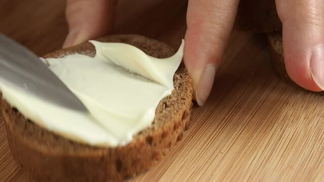 woman's hand spreads butter or soft cheese on slices of rye bread
