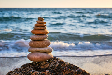 Fototapeta na wymiar Concept of balance and harmony. Cairn stack of stones pebbles cairn on the beach coast of the sea in the nature on sunset. Meditative art of stone stacking