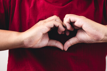 Person shows hands sign of love near the chest. The man with red shirt in medium close up shot.