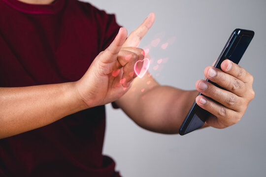 Valentine's day concept. Person uses hand to give love thru a smartphone. Heart shape in visual effect.