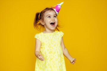 Happy baby girl in princess hat at birthday party spread her arms up screaming isolated on yellow...