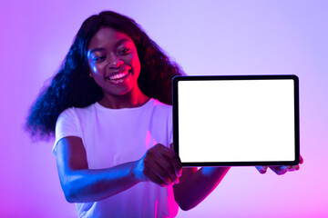 Millennial African American lady presenting mockup for advertisement on tablet screen in neon light, selective focus