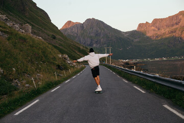 Young man ride on longboard on empty mountain road. Millennial freedom and outdoor vibes lifestyle. Skateboarding culture