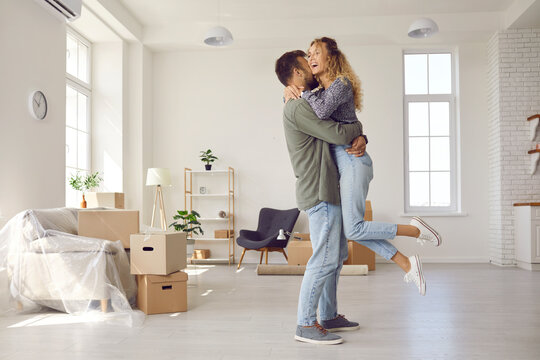 Happiness in new home. Happy married couple is having fun, hugging and sincerely rejoicing over moving to new home. Family in interior of new living room. Mortgage, people and real estate concept