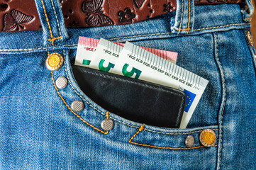 Black leather wallet with euro banknotes looks out of the pocket of jeans