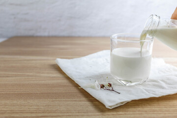 pouring tasty milk into milk glass on wooden table in morning