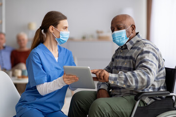 Female nurse helping black senior man using digital tablet