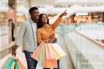 Portrait of black couple with shopping bags pointing at window