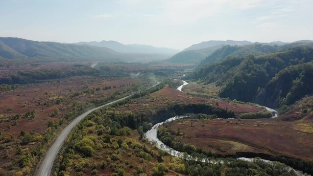 Mountain road and winding river in  mountains gorge, autumn landscape, red leaves, aerial drone view