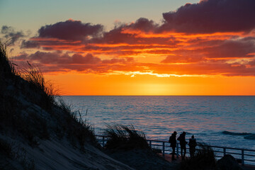 3 Menschen beobachten den Sonnenuntergang am Meer